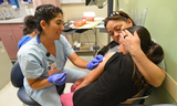 Medical technician in scrubs smiling warmly and giving a shot to a girl in her mom's arms