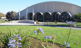 Arched entrance to San Mateo County Event Center with grass and flowers in foreground